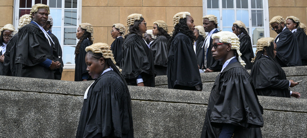 Lawyers in traditional black gowns and light-colored wigs walk up a winding concrete ramp as they arrive at the Supreme Court of Kenya, in Nairobi, to be admitted to the Bar in November 2023. Some are also wearing sunglasses.