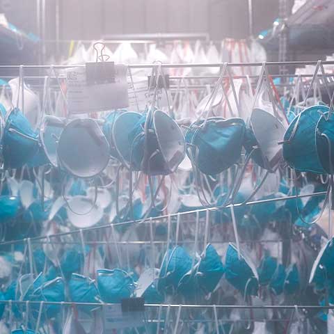 Face masks, used to protect against COVID-19, are worn inside a mobile decontamination unit in Columbus, Ohio. Hundreds of masks hang from rods as they are automatically decontaminated. The air around them is cloudy.