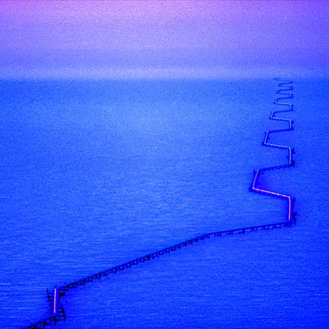 Aerial photo of the Trans-Alaska Pipeline. The raised pipeline zig-zags across the dimlylit, snow-covered tundra in North Slope, Alaska. The pipeline starts the bottom of the image and can be seen until it meets the horizon.  