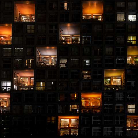 A nighttime image of the outside of a building on the artificial island of Odaiba in Tokyo Bay. Windows in the common areas of the building are lit up and form patterns that look like ascending steps. 