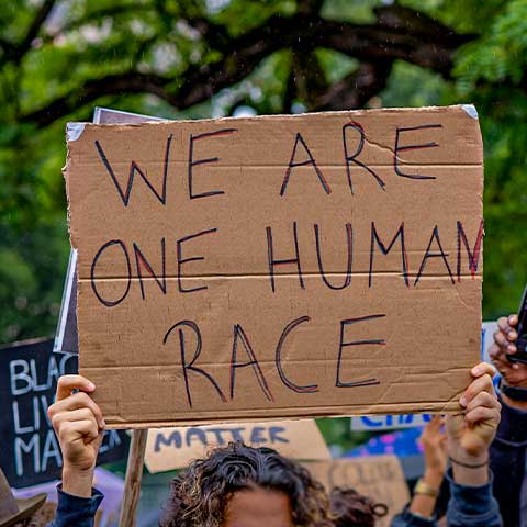 A closeup of a handmade cardboard sign that says "WE ARE ONE HUMAN RACE." Other signs are partially visible in the background at this protest against racism in Stuttgart, Germany.