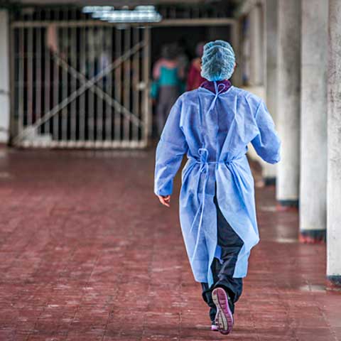 A photo from the back of a healthcare worker in protective gear walking towards a group of inmates behind metal bars in a women's prison in Colombia. 