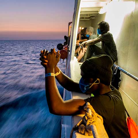 A photo of people leaning against the railings  at sunset on board the SeaWatch 4 rescue ship carrying more than 350 migrants cheer after learning they could land in Palermo, Italy.