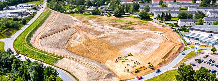 An aerial view of a rehabilitated waste dump in Bad Schlema, Germany. More than one million tons of soil were removed from the former dump, leaving a flat expanse of dirt on which houses will be built. A road, grass, trees and buildings surround the site.