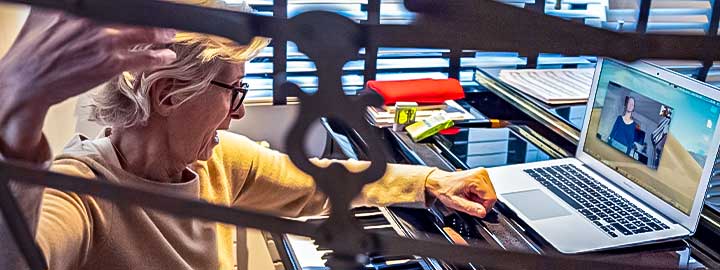 A photo of a professor of voice at a Paris music conservatory teaching an online class in front of a keyboard and laptop.