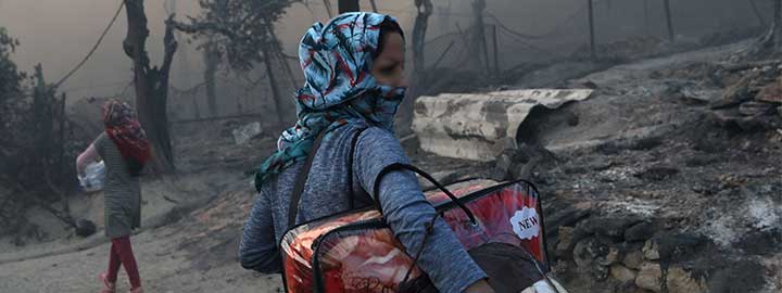 A migrant woman carries her belongings through a smoky, burnt landscape after a fire at the Moria camp for refugees and migrants on the island of Lesvos, Greece.