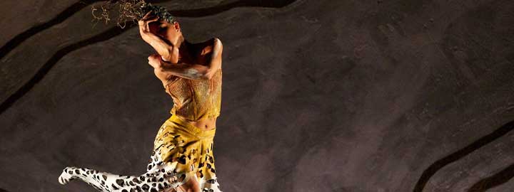 A photo of Ella Havelka dancing on a dramatically lit stage in an orange and white spotted flowing gown in the Frances Rings-choreographed work 'Terrain'. 