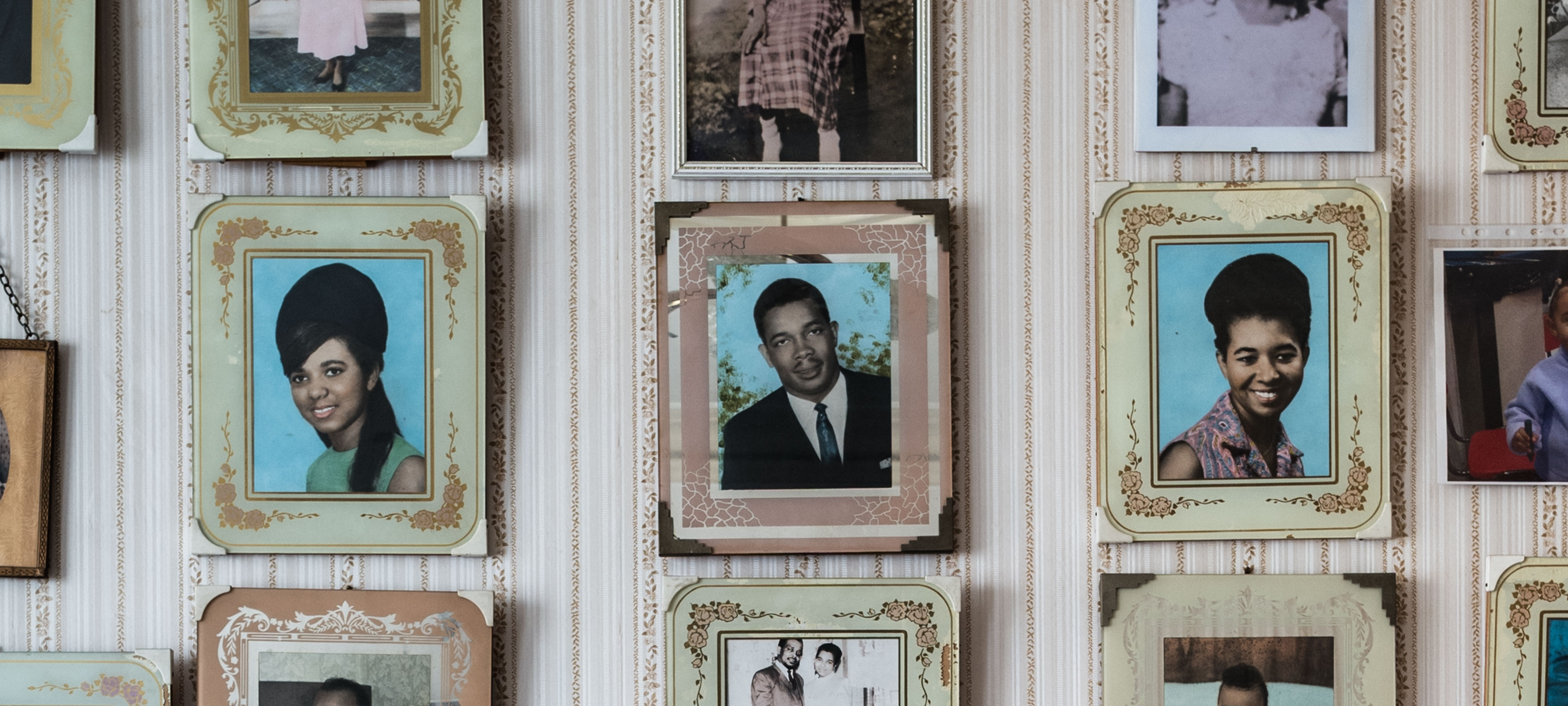 Family portraits hung on a wall in a Jamaican home in London in pastel frames with distinctive flower designs like those profiled by photographer Jim Grover in his 2018 exhibit "Windrush: Portrait of a Generation."