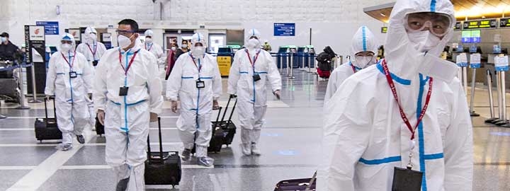 Airline crew members dressed in protective suits arrive at Los Angeles International Airport. They are masked and pulling their luggage behind them inside the airport.