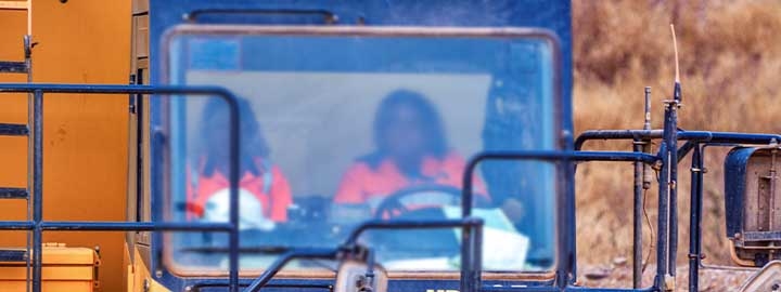 A view of the front of a truck driven by a woman working at a gold mining site in Burkina Faso. Taken through the truck’s front window, the image shows the driver and her co-worker, who is in the passenger seat. 
