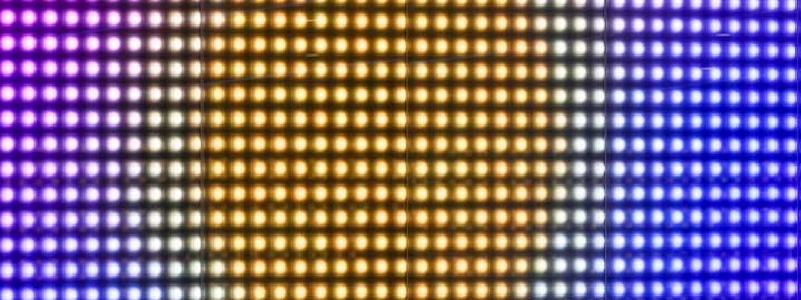 This close-up image of an LED display along Wembley Way in London shows rows of small circles of brightly colored lights. The colors form a pattern that resembles the sun at the center, surrounded by hazy glow that is, in turn, surrounded by cooler-toned lights that resemble the sky.