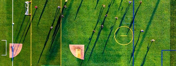An aerial view of a soccer field in Long Beach, NY. Players on the field appear as dots and cast long shadows across the field. 