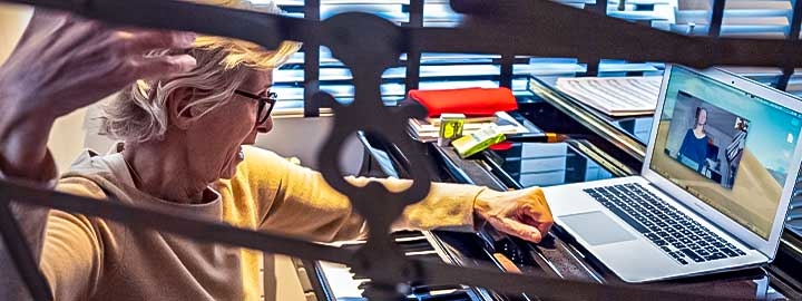 A photo of a professor of voice at a Paris music conservatory teaching an online class in front of a keyboard and laptop.