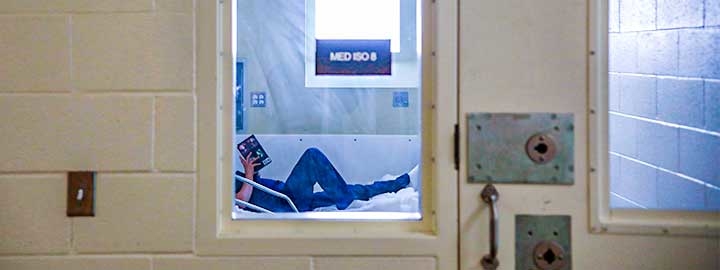 A photo of an inmate reading a book on a bed in the infirmary of a women's prison in California. 