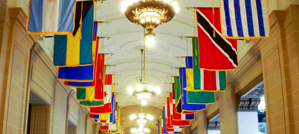 The white, arched paneled ceiling of the Hall of Heroes at the headquarters of the Organization of American States lined with the flags of the Member States.