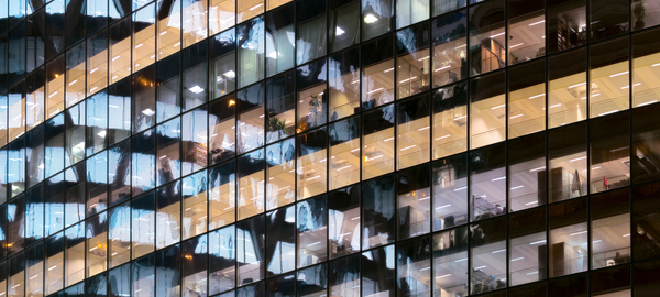 A closeup shows several floors of the exterior of a building in Paris, with offices inside. Outside, abstract reflections are visible in the building’s glass facade. 
