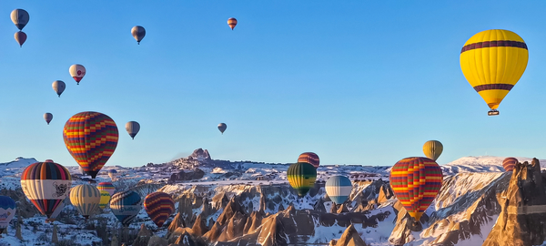 Colorfully striped hot-air balloons float over snow-covered rock formations called fairy chimneys in the Cappadocia region of Turkey.