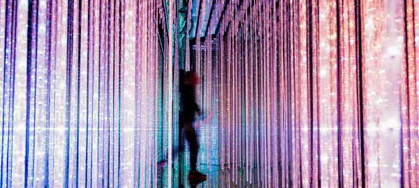 A man strolls through floor-to-ceiling strips of colorful lights
