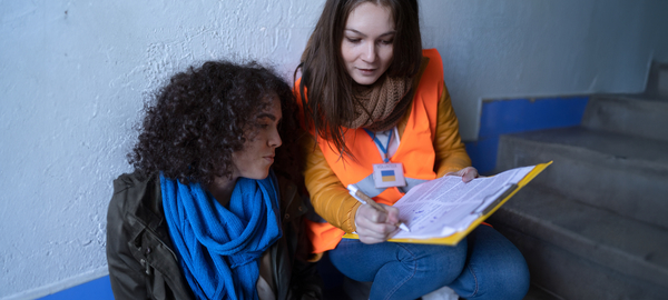 A female volunteer, right, and Ukrainian refugee woman, left, sit on steps in a train station, both looking at a document the volunteer is holding and explaining