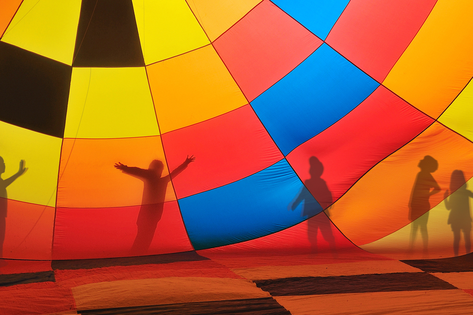 Silhouettes of five children playing outside a colorful hot air balloon.