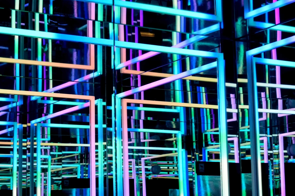 Overlapping turquoise, blue, purple and peach neon lights in geometric public art installation with mirrored backdrop