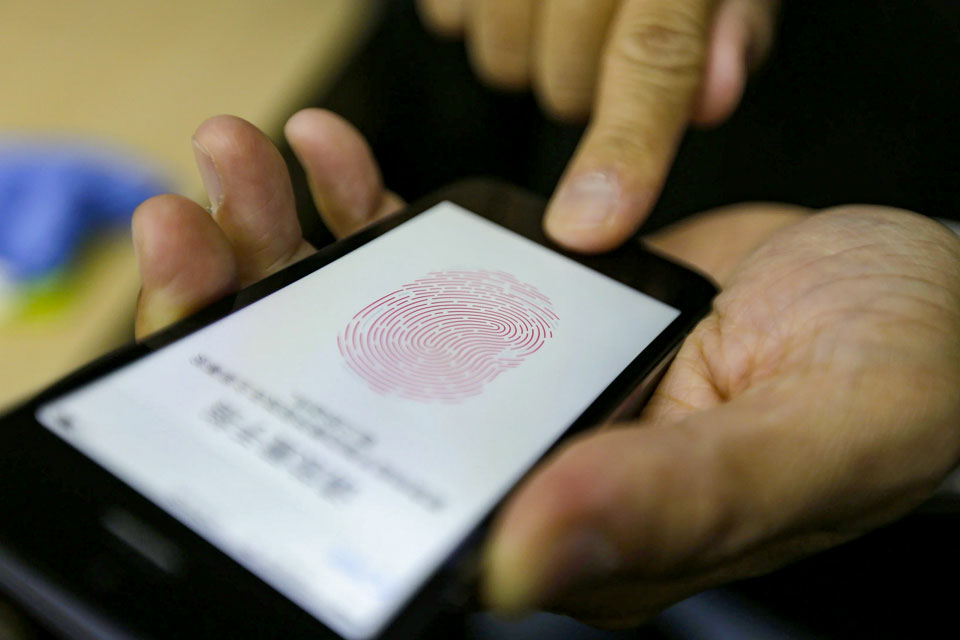 A close-up of hands holding a mobile phone with the screen displaying the image of a fingerprint as the person uploads their biometric data in the form of their fingerprint.