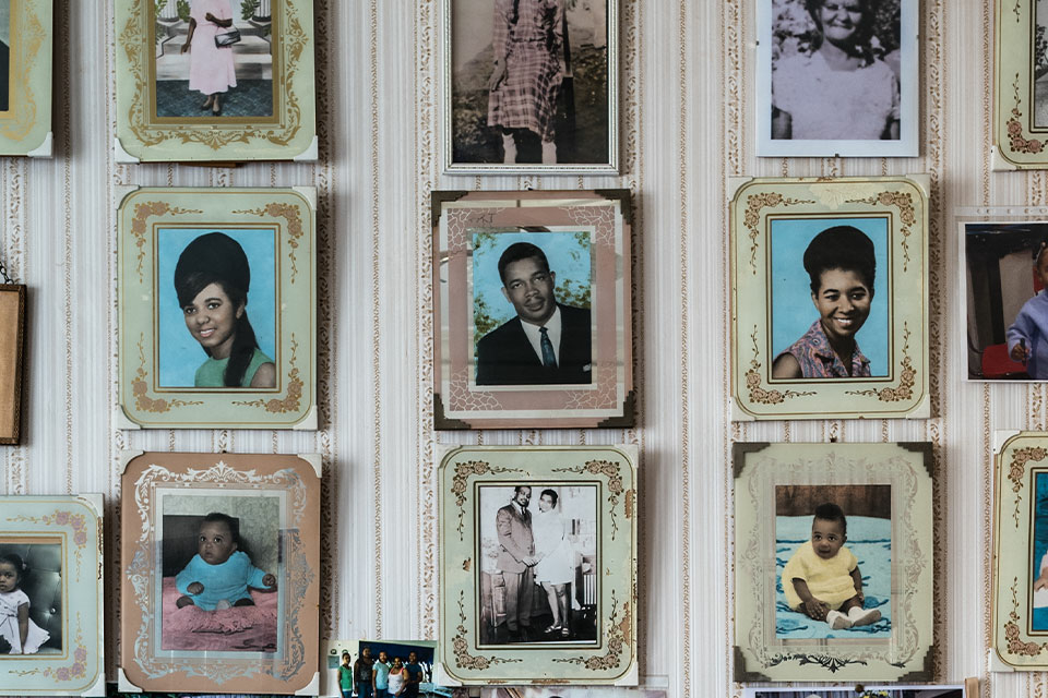 Family portraits hung on a wall in a Jamaican home in London in pastel frames with distinctive flower designs like those profiled by photographer Jim Grover in his 2018 exhibit "Windrush: Portrait of a Generation."