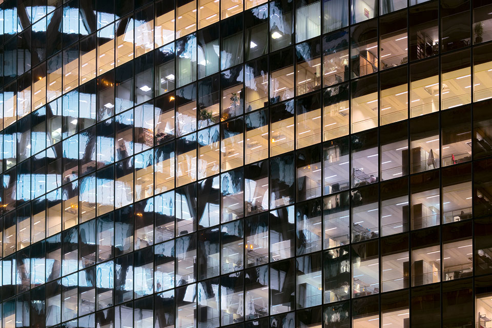 A closeup shows several floors of the exterior of a building in Paris, with offices inside. Outside, abstract reflections are visible in the building’s glass facade. 