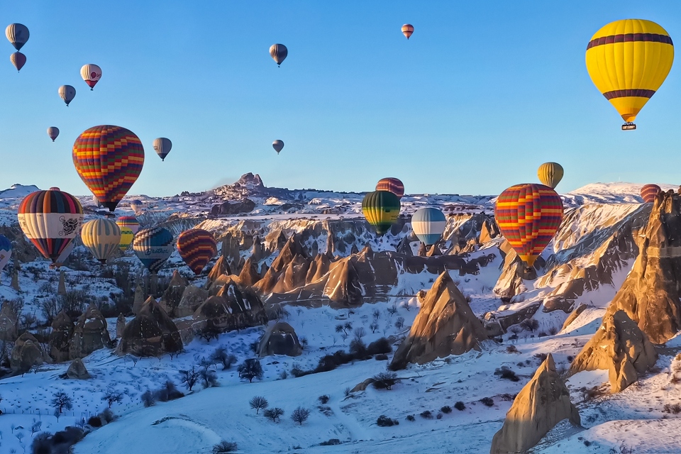 Colorfully striped hot-air balloons float over snow-covered rock formations called fairy chimneys in the Cappadocia region of Turkey.