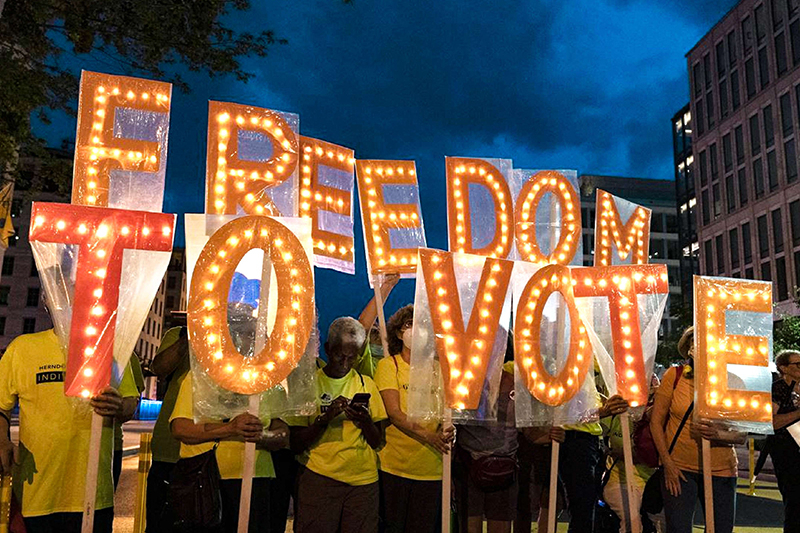 Voting rights activists during a rally at Black Lives Matter Plaza in Washington, DC hold up large individual orange letters emblazoned with light bulbs that spell out the words Freedom to Vote.