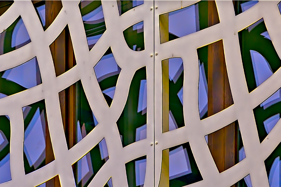 Three colorful windows on a building in Romania that was designed using geometric patterns, with an opening in each windowpane. The windows are located one behind the other.