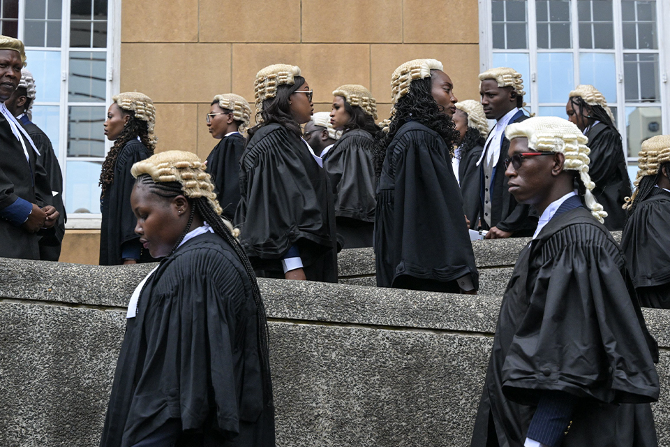 Lawyers in traditional black gowns and light-colored wigs walk up a winding concrete ramp as they arrive at the Supreme Court of Kenya, in Nairobi, to be admitted to the Bar in November 2023. Some are also wearing sunglasses.