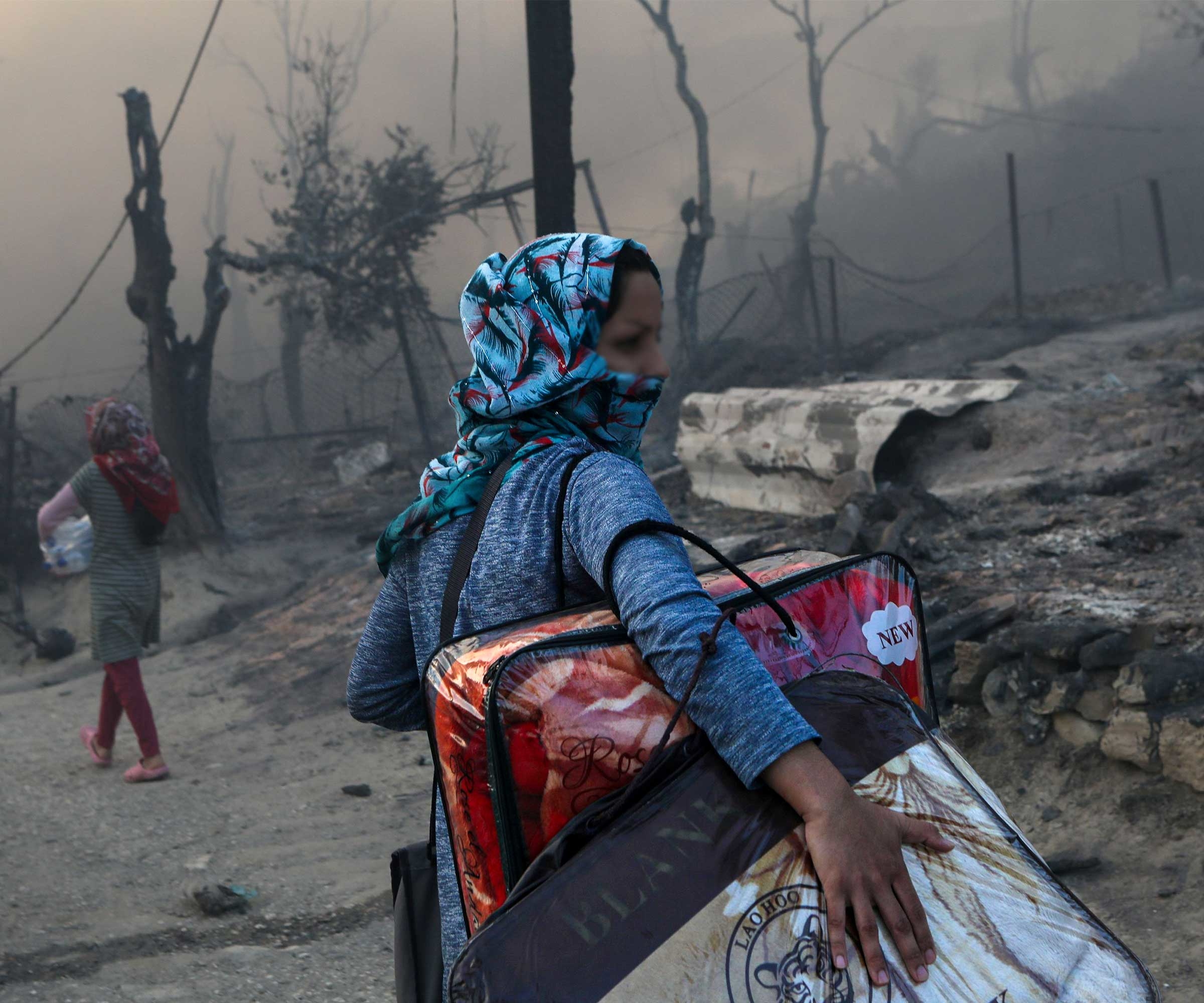 A migrant carries her belongings after a fire at the Moria camp for refugees and migrants on the island of Lesvos, Greece. © Elias Marcou/Reuters