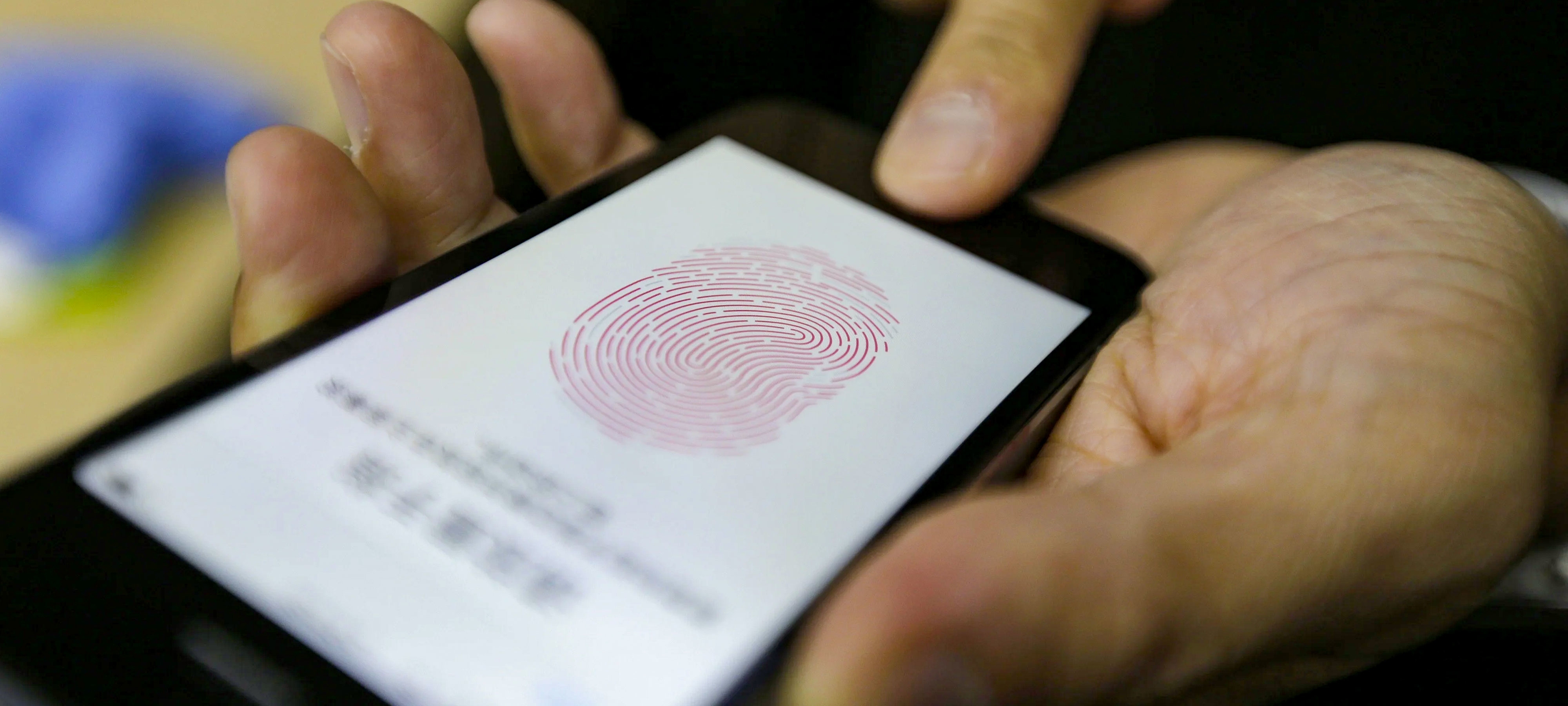 A close-up of hands holding a mobile phone with the screen displaying the image of a fingerprint as the person uploads their biometric data in the form of their fingerprint.