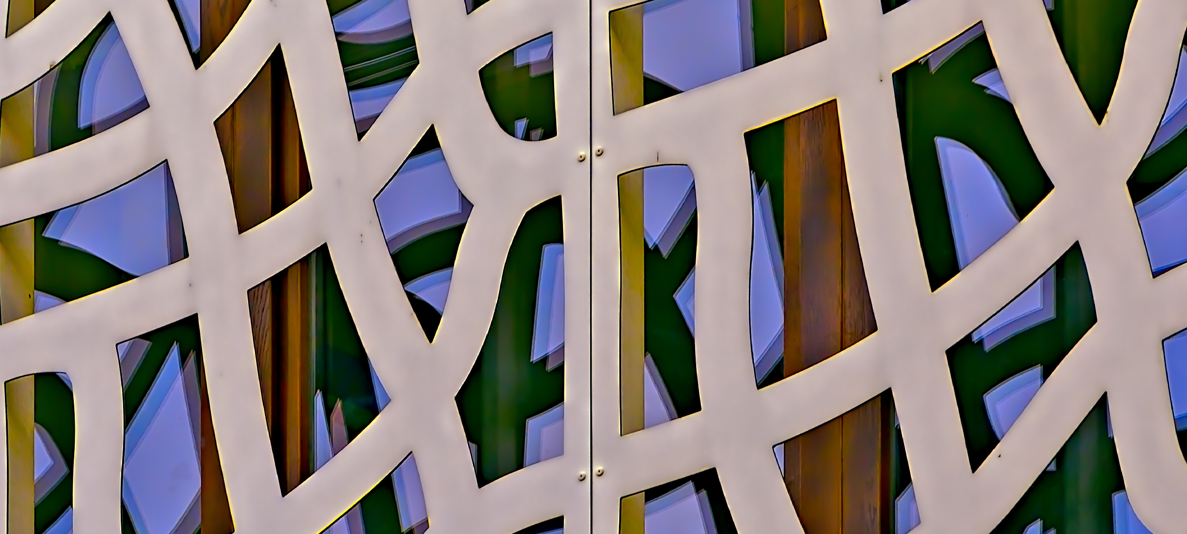 Three colorful windows on a building in Romania that was designed using geometric patterns, with an opening in each windowpane. The windows are located one behind the other.