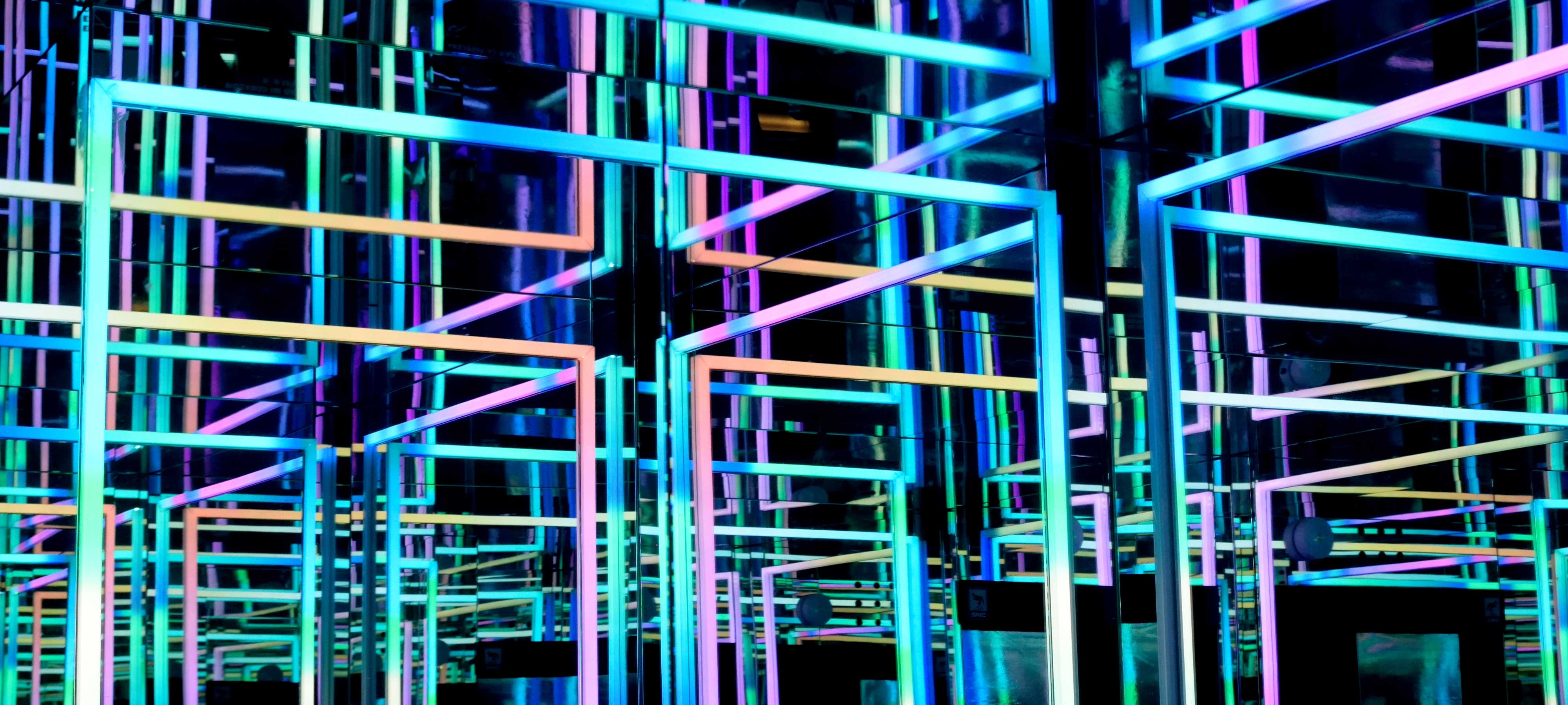 Overlapping turquoise, blue, purple and peach neon lights in geometric public art installation with mirrored backdrop