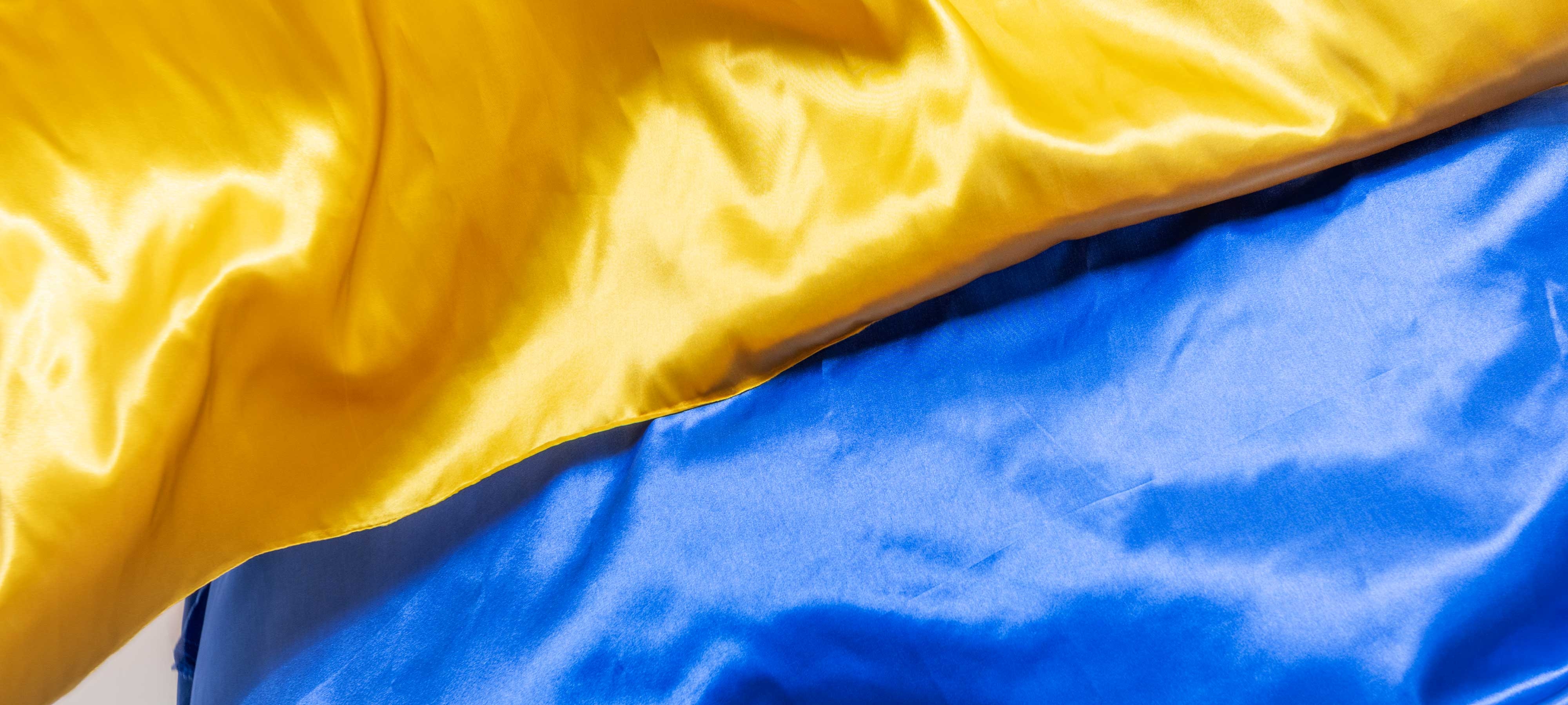 Two satin fabrics—one yellow and one blue, matching the colors of the Ukrainian flag—are partially sewn together.